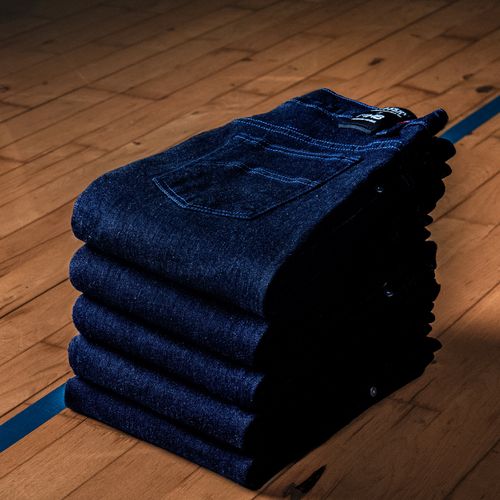 Pile de jeans bruts Atelier Tuffery sur parquet en bois, savoir-faire français - Atelier Tuffery