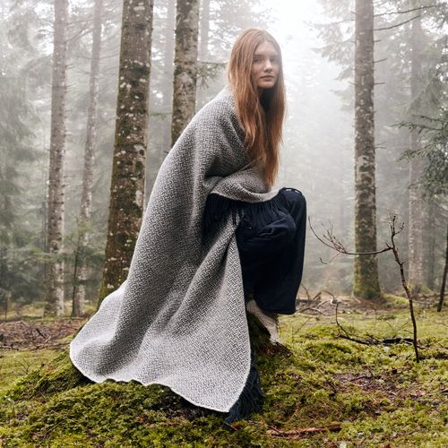 Couverture en laine Atelier Tuffery portée par une femme en forêt, ambiance naturelle et brumeuse - Atelier Tuffery