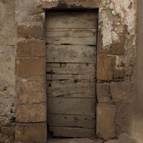 Vieille porte en bois cloutée encastrée dans un mur en pierre, à l’entrée d’un bâtiment abandonné - Atelier Tuffery