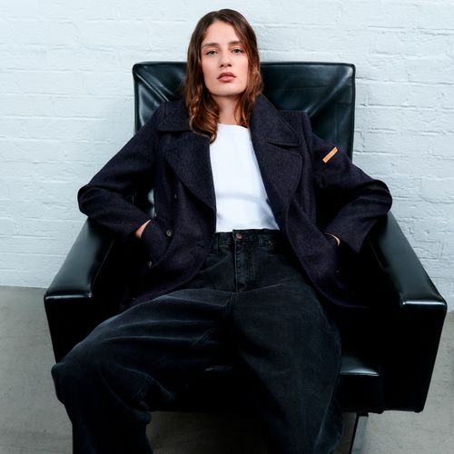 Femme en manteau long bleu marine Atelier Tuffery, assise sur fauteuil noir, collection automne-hiver 2025-2026 - Atelier Tuffery