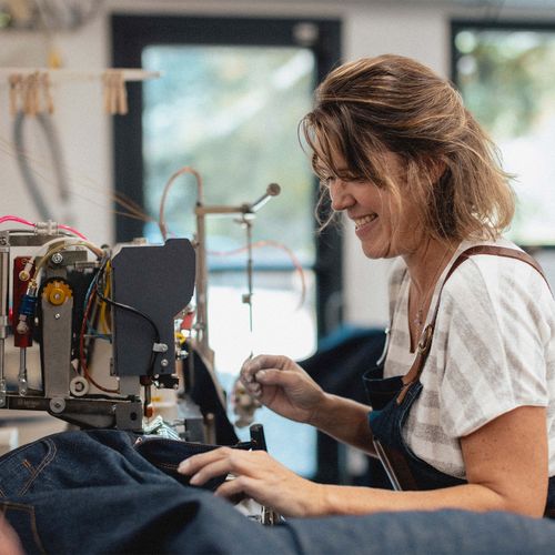 Couturière souriante travaillant sur un jean à l’atelier Tuffery - Atelier Tuffery