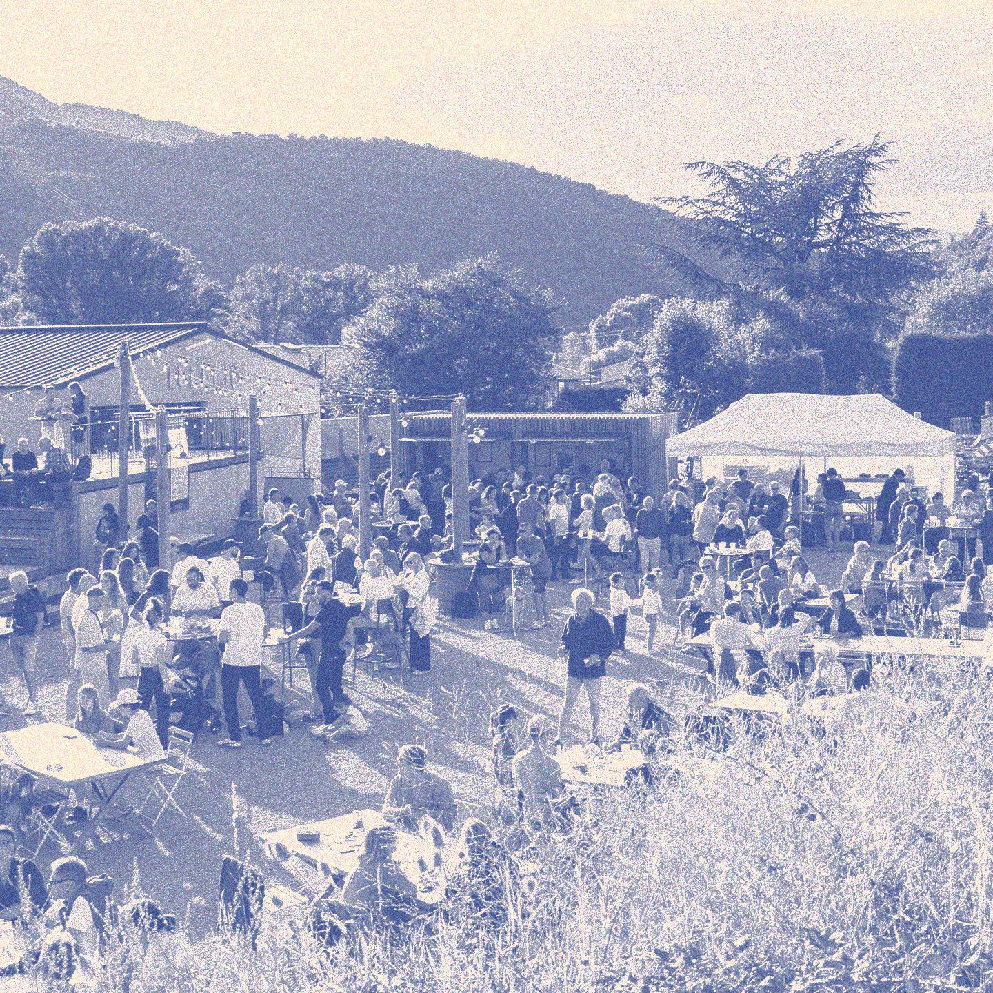 Vue panoramique des Heures Bleues chez Atelier TUFFERY. Des centaines de visiteurs profitent d'une soirée estivale en plein air avec restauration, musique et animations dans un cadre naturel au pied des montagnes lozériennes. | Atelier Tuffery