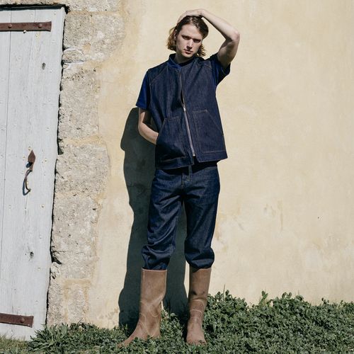 Homme portant une tenue en denim brut et des bottes, devant un mur de pierre à Cavaladette. - Atelier Tuffery