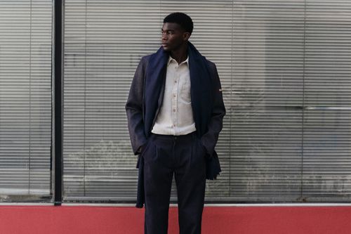 Un homme avec un manteau, un pantalon à plis en laine, une chemise écru et une écharpe marine - Atelier Tuffery