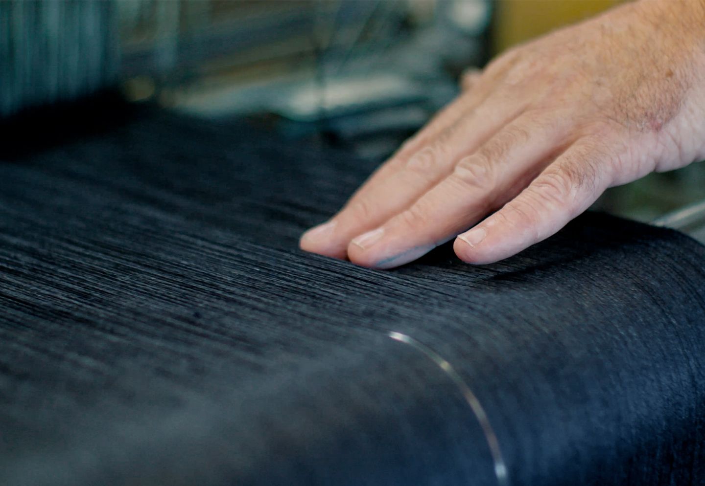 Main posée sur un tissage de toile sombre intégrant de la laine locale, étape de transformation de la matière. | Atelier Tuffery