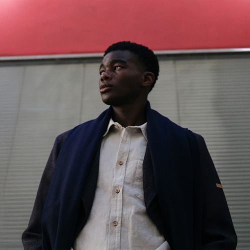 Un homme avec un manteau, un pantalon à plis en laine, une chemise écru et une écharpe marine - Atelier Tuffery