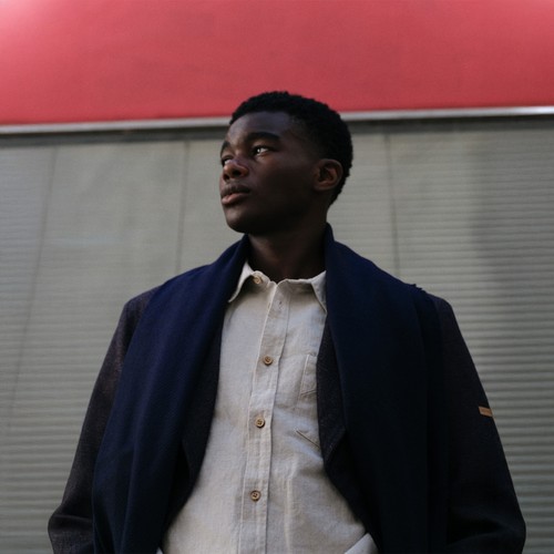 Un homme avec un manteau, un pantalon à plis en laine, une chemise écru et une écharpe marine - Atelier Tuffery
