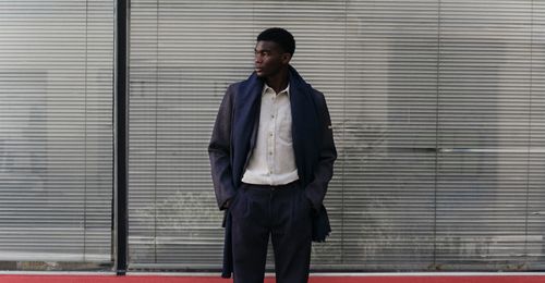 Un homme avec un manteau, un pantalon à plis en laine, une chemise écru et une écharpe marine - Atelier Tuffery