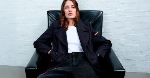 Femme en manteau marine et jean noir assise dans un fauteuil - Atelier Tuffery