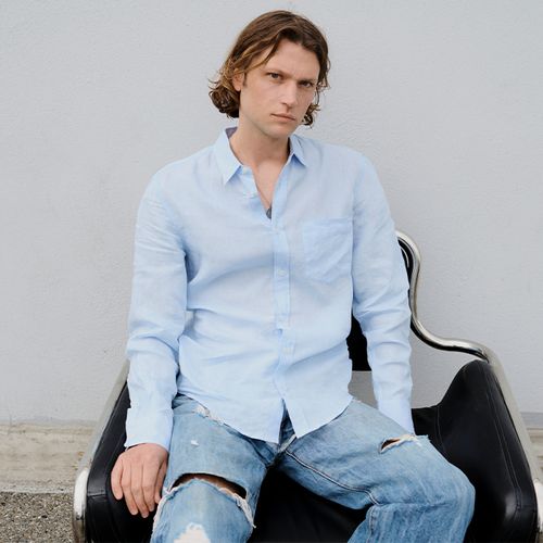 Homme assis portant une chemise bleu clair et un jean délavé déchiré. - Atelier Tuffery