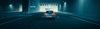 A car drives through a dimly lit tunnel with blue lighting, heading towards a bright exit.
