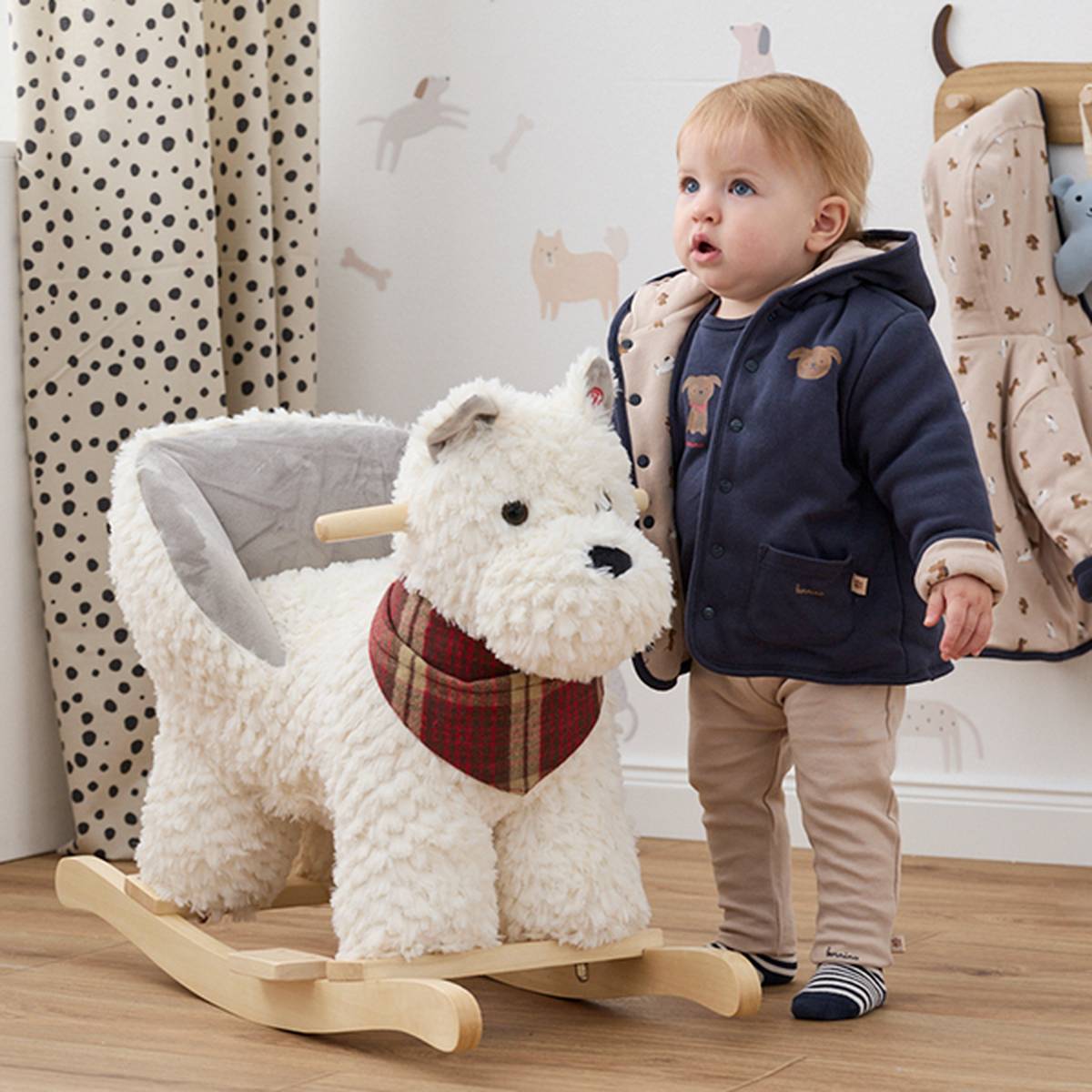 Ein Bild von einem Kleinkind in einer Winterjacke neben einem Schaukelhund