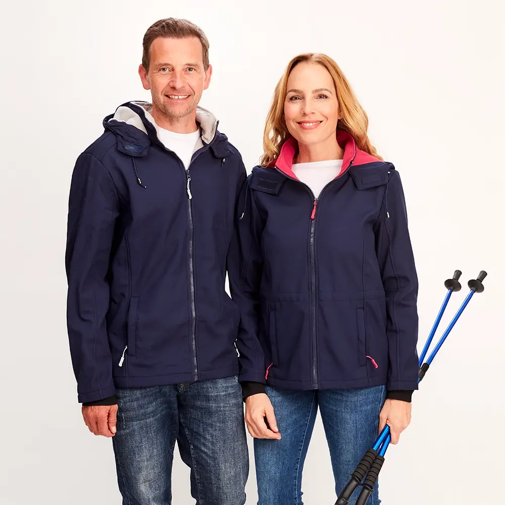 Ein lächelnder Mann und eine lächelnde Frau in passenden marineblauen Jacken stehen mit Wanderstöcken vor einem weißen Hintergrund.