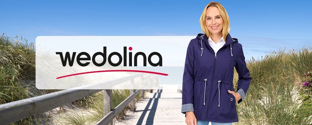 Eine Frau in einer blauen Jacke steht unter strahlend blauem Himmel neben Strandgras und einem Holzsteg, im Vordergrund ist das „Wedolina“-Logo zu sehen.
