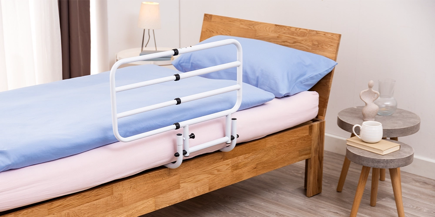 Ein Holzbett mit blau-rosa Bettwäsche und einem weißen Schutzgitter. Auf einem Beistelltisch stehen eine Vase, ein Glas und eine Tasse.