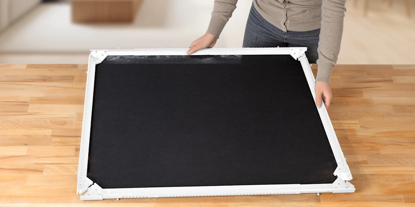 Eine Person, die auf einem Holztisch das Insektenschutzgitter mit einem weißen Rahmen zusammenbaut.