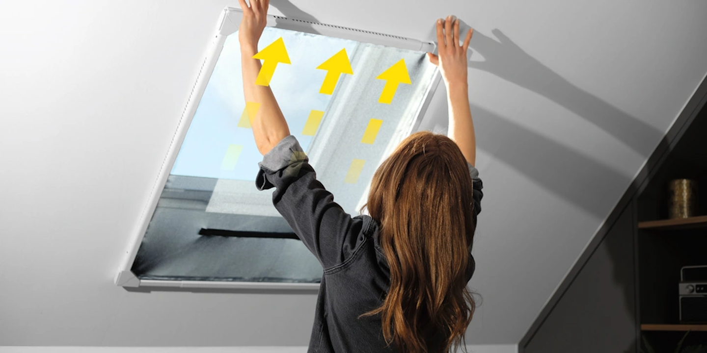 Eine Person montiert das Moskitonetz an einem Dachfenster; gelbe Pfeile zeigen die variable Größenanpassung an. Licht fällt durch das geöffnete Fenster herein.