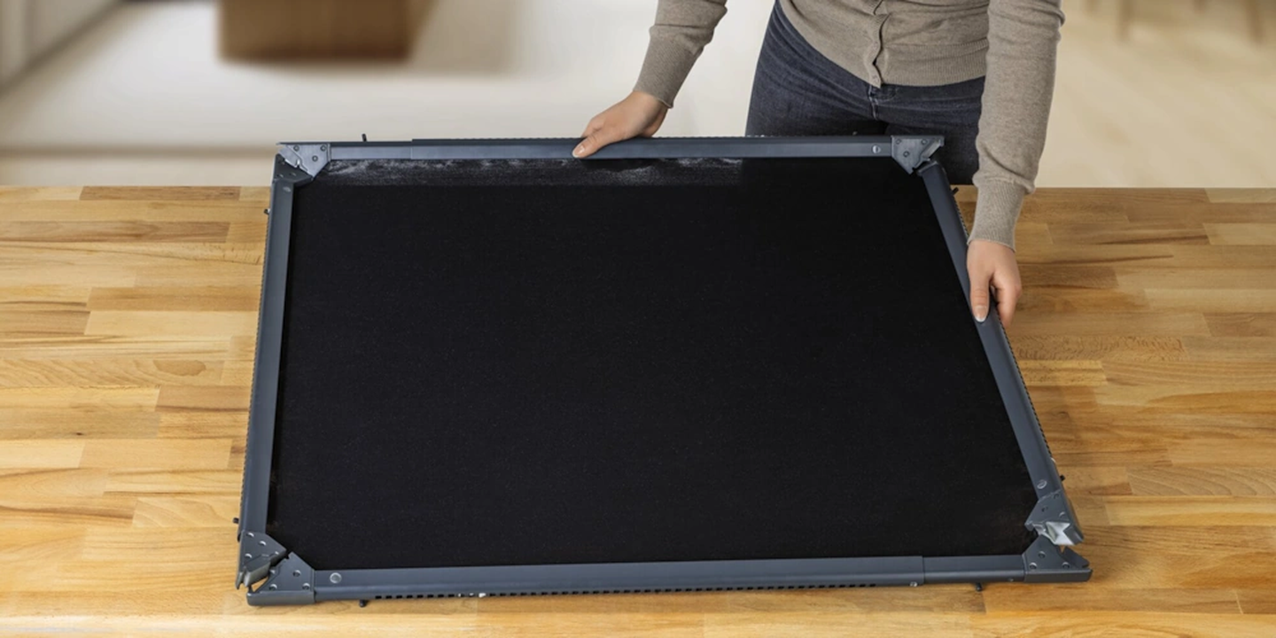 Eine Person, die auf einem Holztisch ein Insektenschutzgitter zusammenbaut.