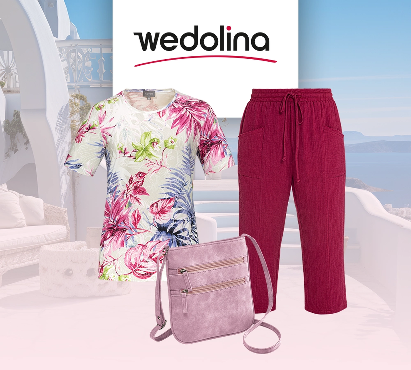 Ein modisches Outfit in Rosa und mit Blumenmuster, dazu eine rosa Tasche vor einer malerischen Küstenkulisse mit blauem Meer, weißen Gebäuden und Topfpflanzen.
