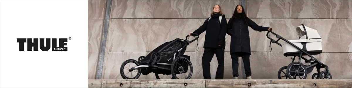Zwei Personen in schwarzen Mänteln stehen mit Thule-Kinderwagen, einem schwarzen und einem weißen, vor einer Steinmauer. Links ist das Thule-Logo zu sehen.