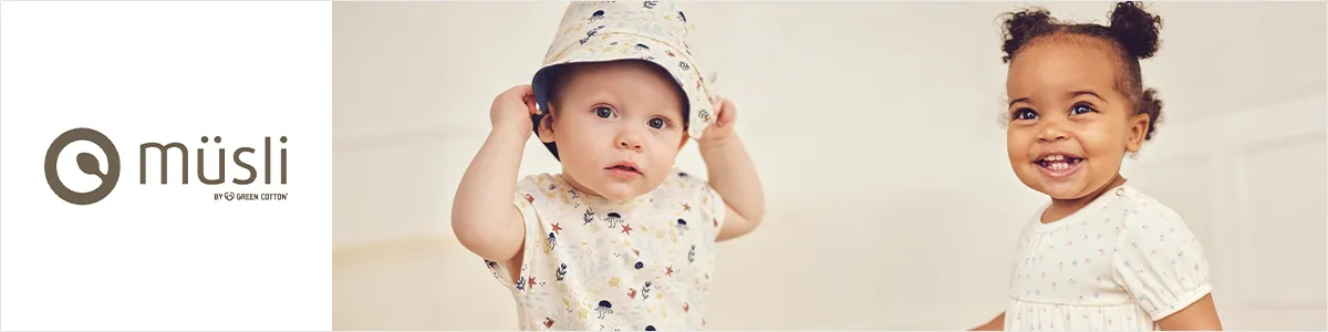 Zwei Kleinkinder in gemusterten Outfits; eines trägt einen Hut, das andere lächelt. „Müsli“-Logo links. Heller Hintergrund.