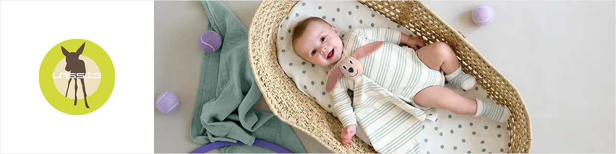 Logo eines Rehs auf einem grünen Kreis neben einem lächelnden Baby in einem gestreiften Strampler, das in einem geflochtenen Korb mit einem Plüschtier liegt.