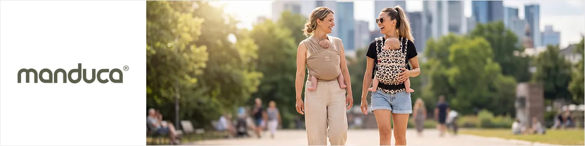 Zwei Frauen spazieren durch einen Park, jede trägt ein Baby in einer Manduca-Babytrage. Im Hintergrund sind üppiges Grün und die Skyline der Stadt zu sehen.