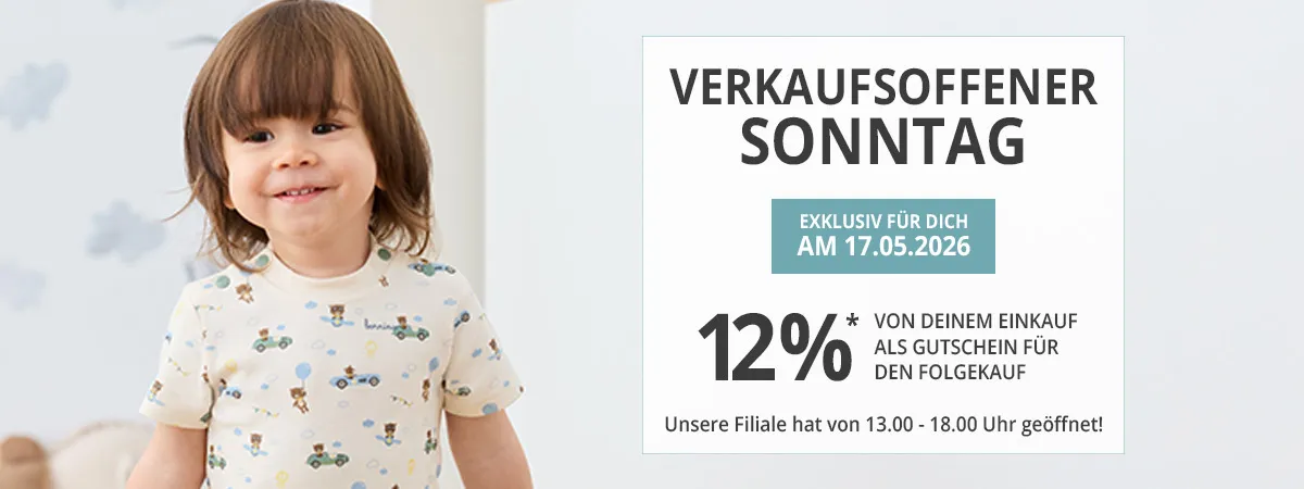 Ein kleines Kind lächelt drinnen neben einer Werbung für eine "Verkaufsoffener Sonntag"-Veranstaltung am 17.05.2026, bei der ein Rabattgutschein über 12%* angeboten wird.