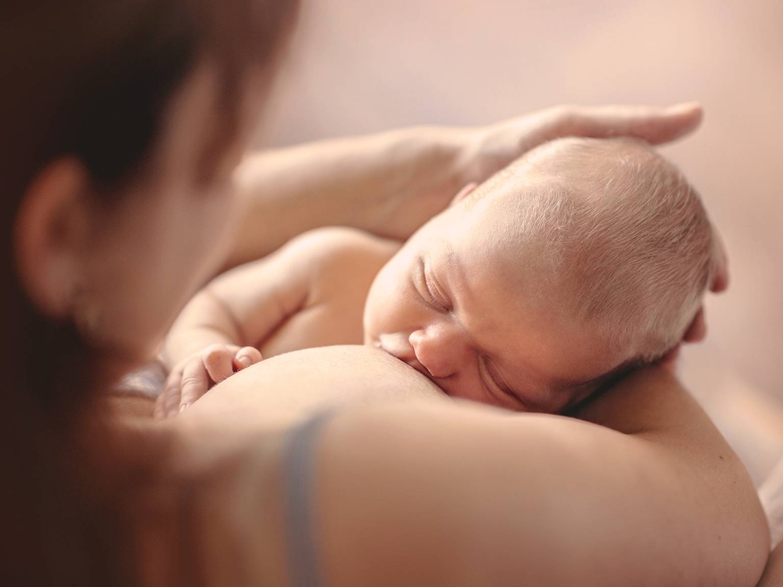 Ein stillendes Baby in den Armen einer Frau, mit einem unscharfen Hintergrund, der eine warme und intime Atmosphäre schafft.