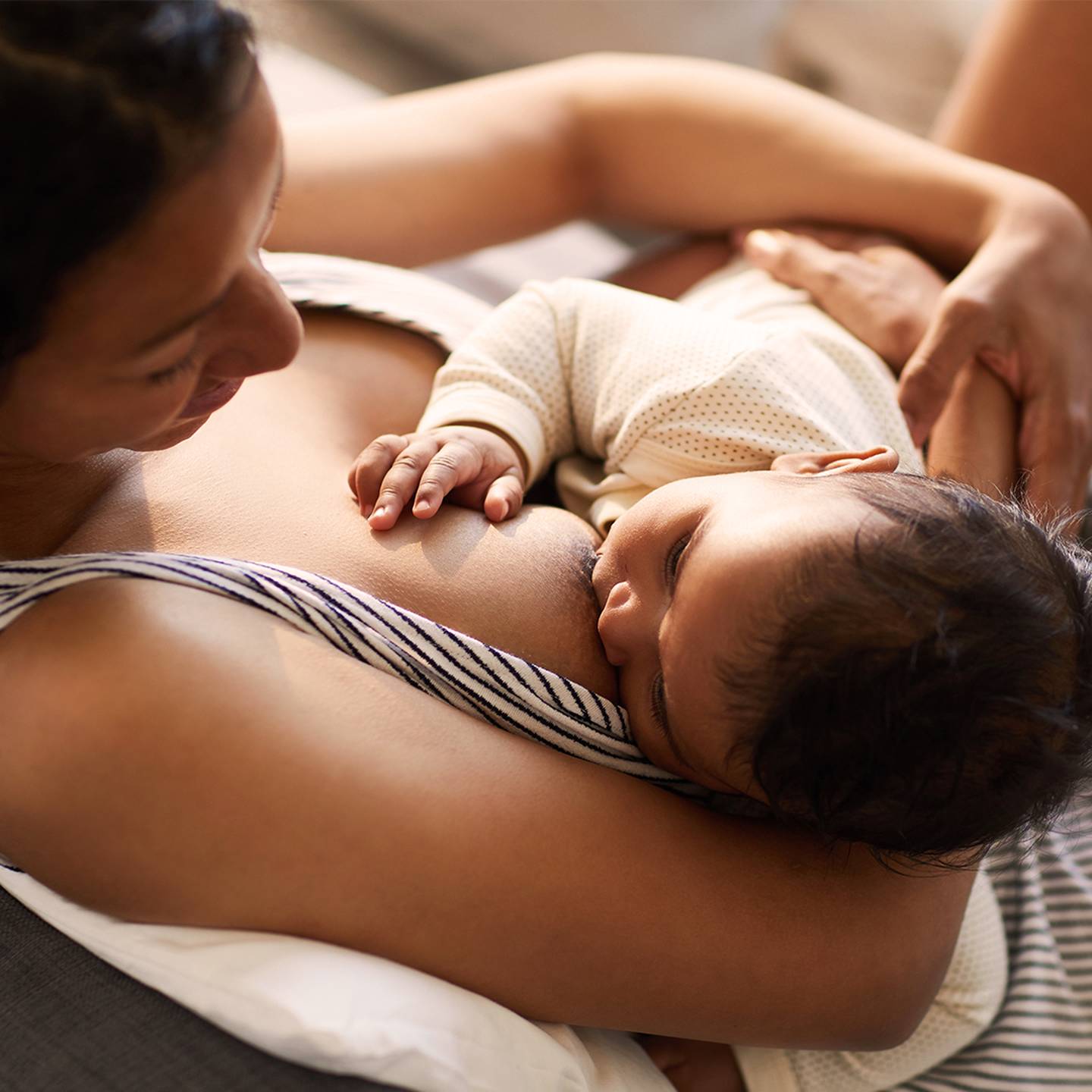 Eine Mutter stillt ihr Baby, während sie auf einem Sofa liegt. Beide sehen in dieser ruhigen Umgebung zufrieden und entspannt aus.