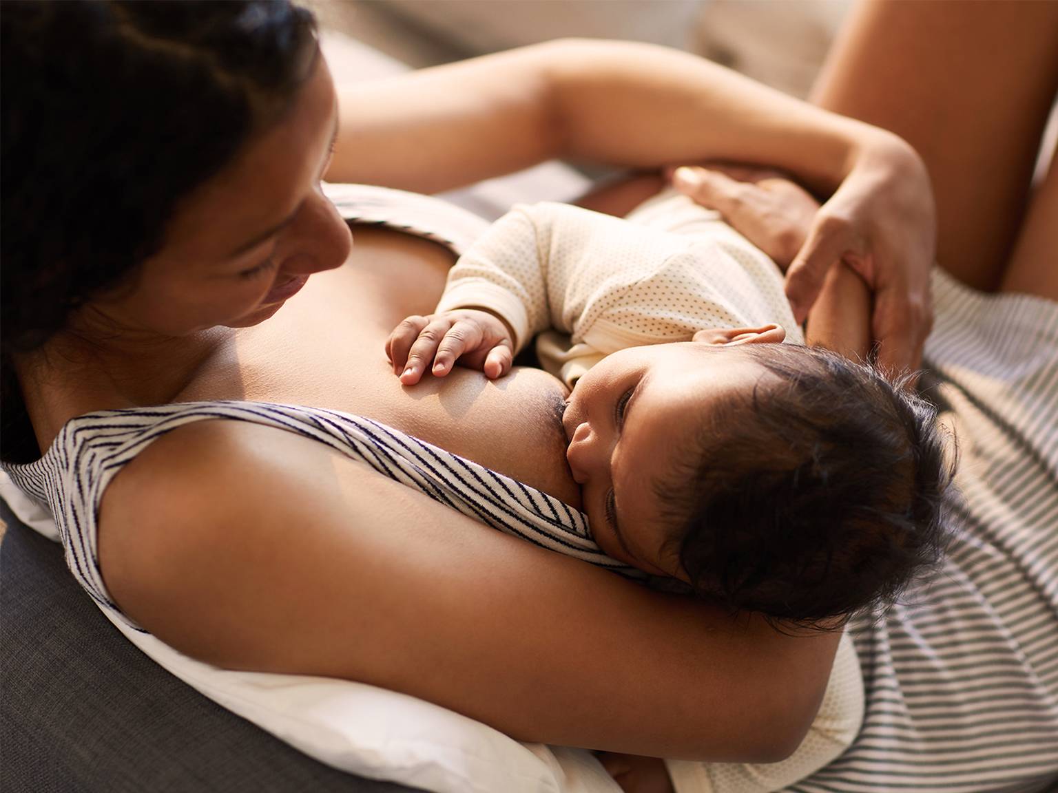 Eine Mutter stillt ihr Baby, während sie auf einem Sofa liegt. Beide sehen in dieser ruhigen Umgebung zufrieden und entspannt aus.