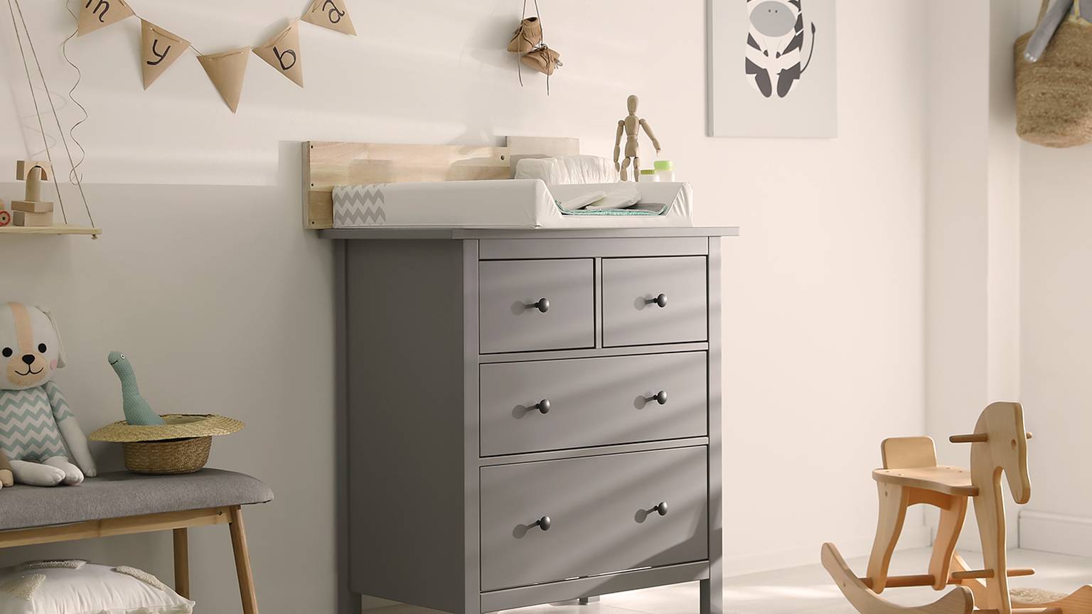 Ein gemütliches Kinderzimmer mit grauem Wickeltisch, Wanddeko, Schaukelpferd und Kuscheltieren. Neutrale Töne schaffen eine beruhigende Atmosphäre.