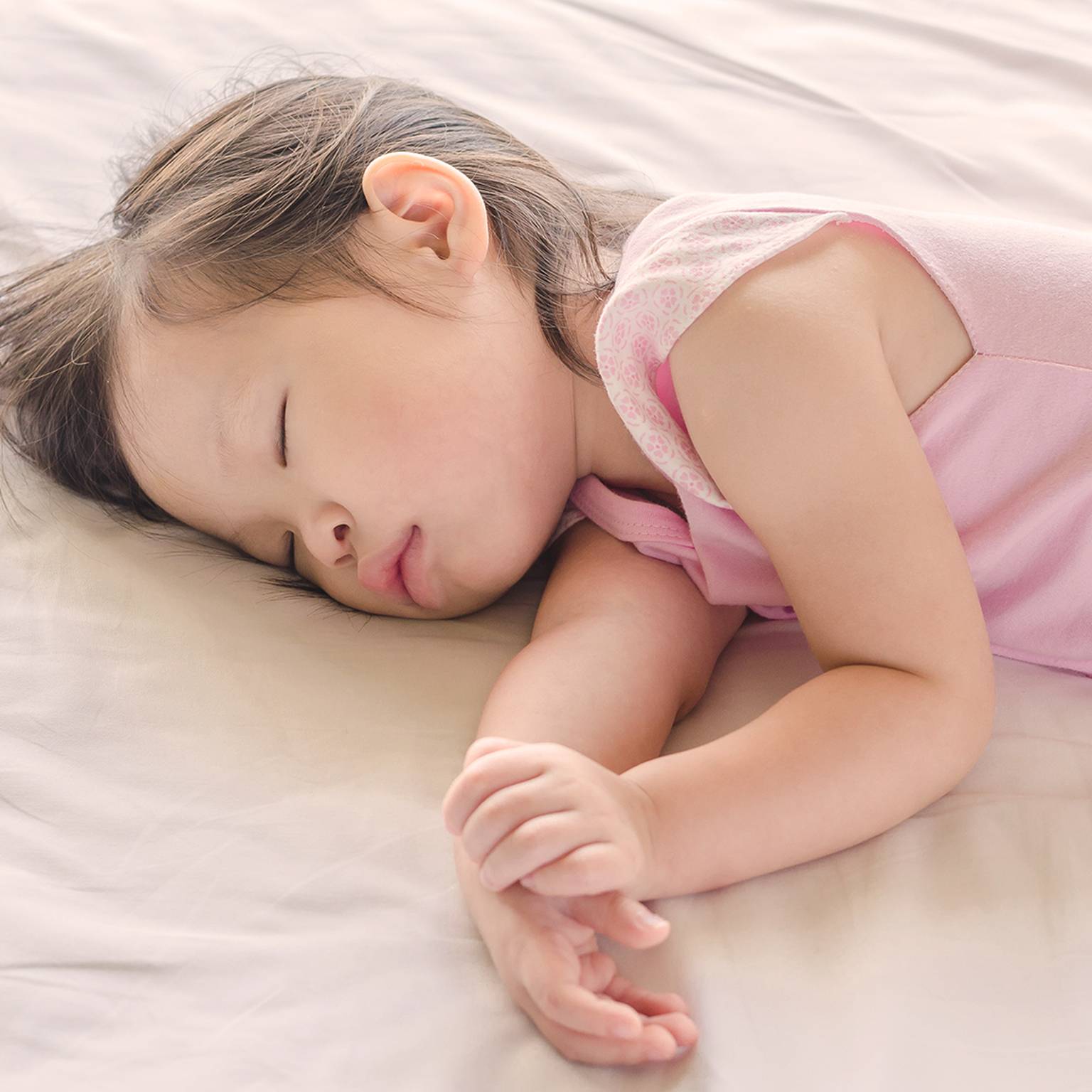 Kleines Kind schläft friedlich in einem Bett, trägt ein rosa Outfit, mit sanfter Beleuchtung und sanften Schatten.