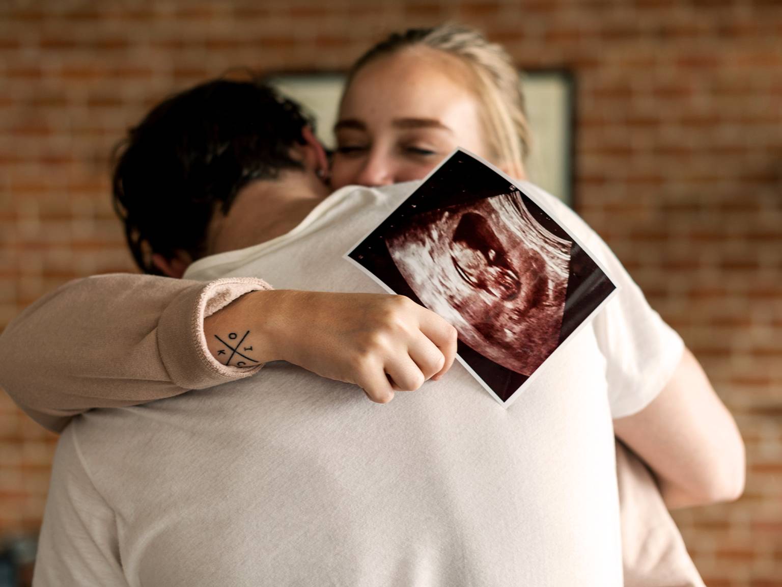 glückliches Paar umarmt sich und zeigt ein Ultraschalbild in die Kamera