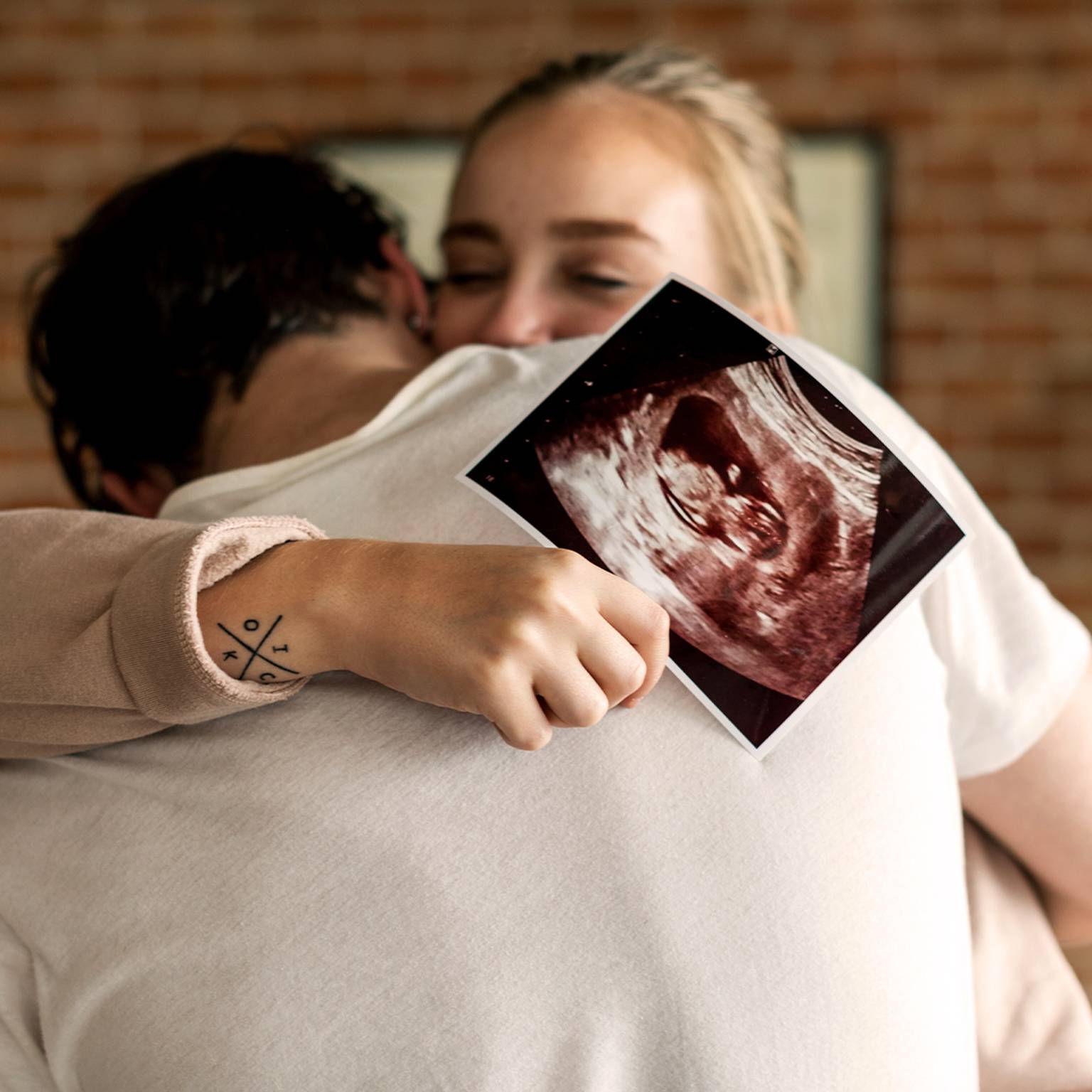 glückliches Paar umarmt sich und zeigt ein Ultraschalbild in die Kamera