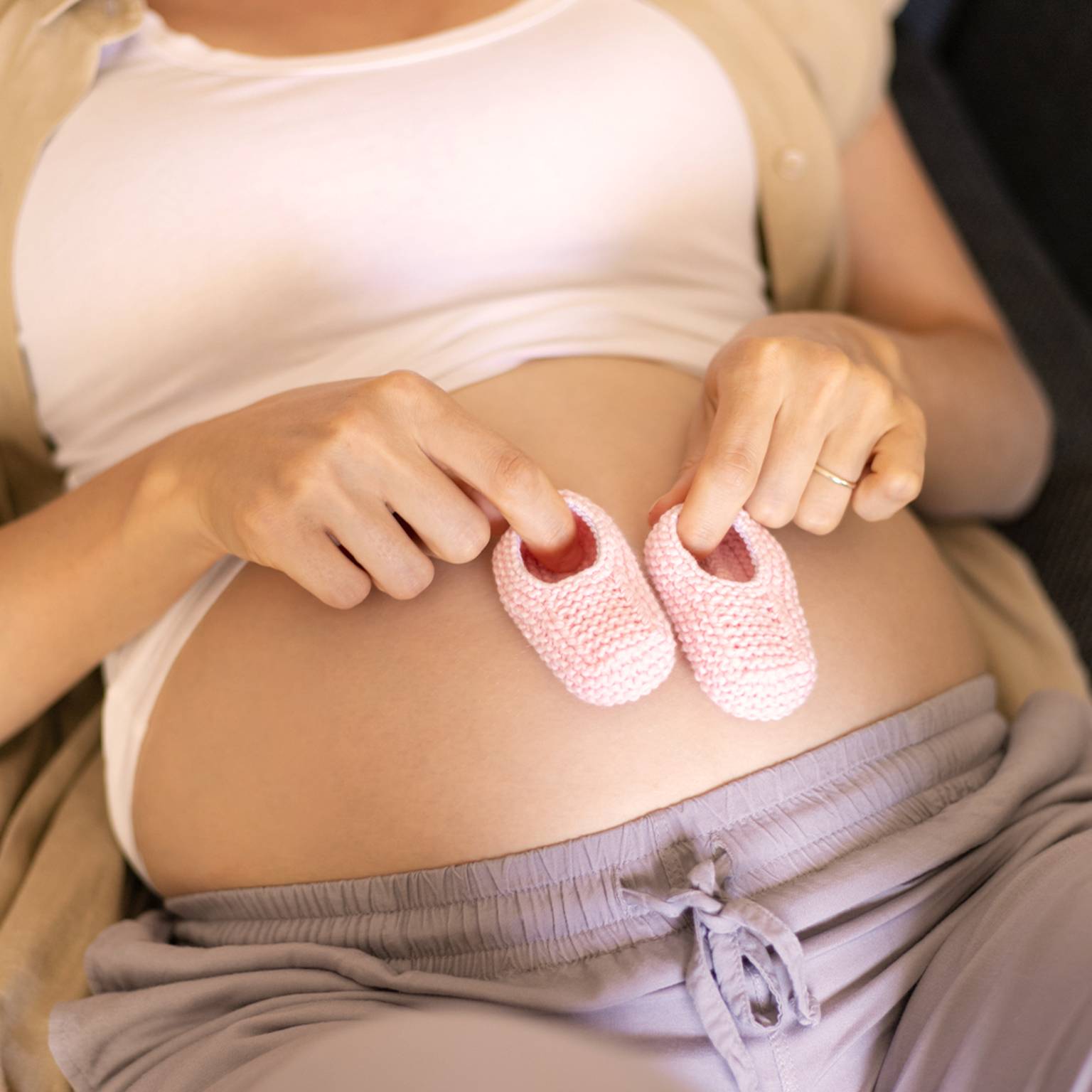 Frau liegt auf dem Rücken und hat kleien Babyschuhe auf ihrem Bauch stehen