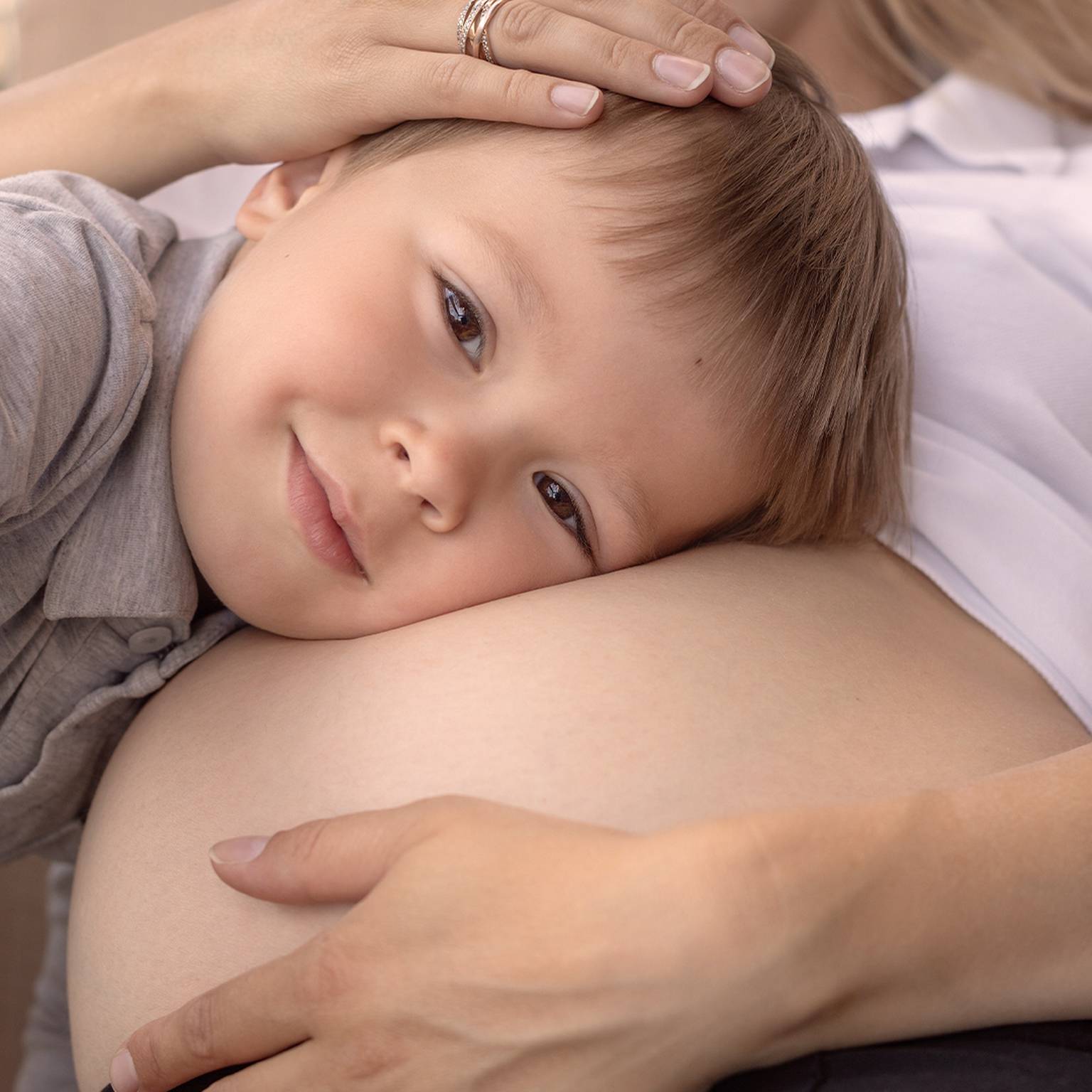 Kleiner Junge liegt fröhlich mit dem Kopf auf dem schwangeren Bauch seiner Mutter