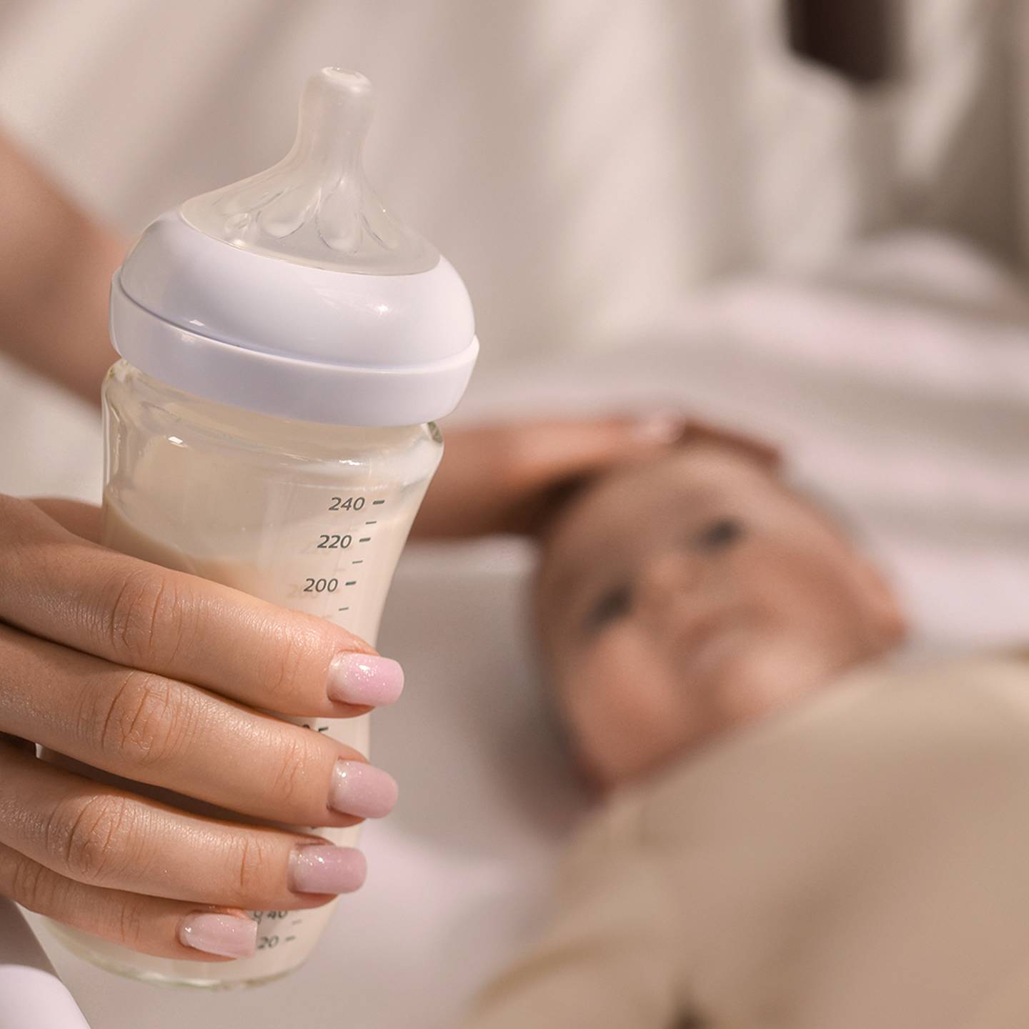 Eine Hand hält eine mit Milch gefüllte Babyflasche neben einem Baby, das in einem Kinderbett liegt, und berührt sanft den Kopf des Babys.