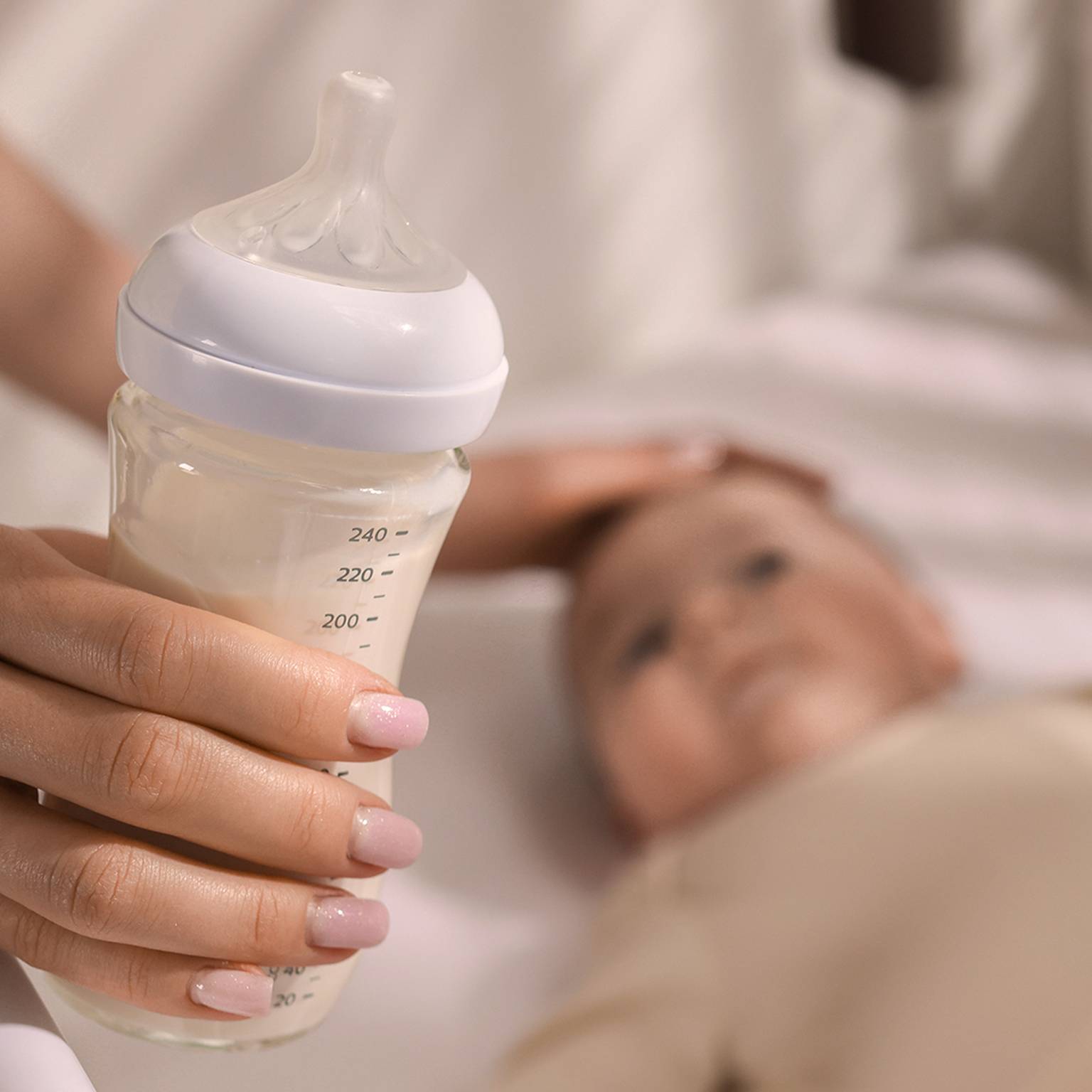 Eine Hand hält eine mit Milch gefüllte Babyflasche neben einem Baby, das in einem Kinderbett liegt, und berührt sanft den Kopf des Babys.