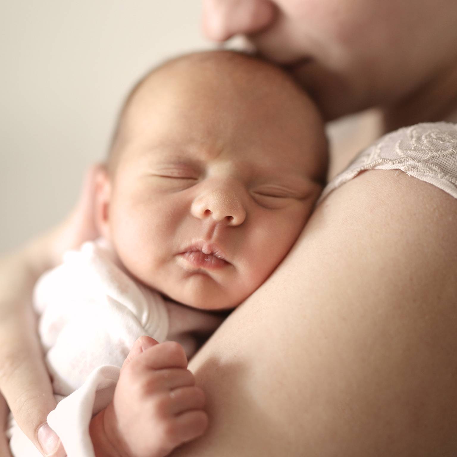 Ein Neugeborenes schläft friedlich auf der Schulter einer Person, eingehüllt in eine weiche weiße Decke. Die Person wiegt das Baby sanft und schafft so eine zärtliche Szene.