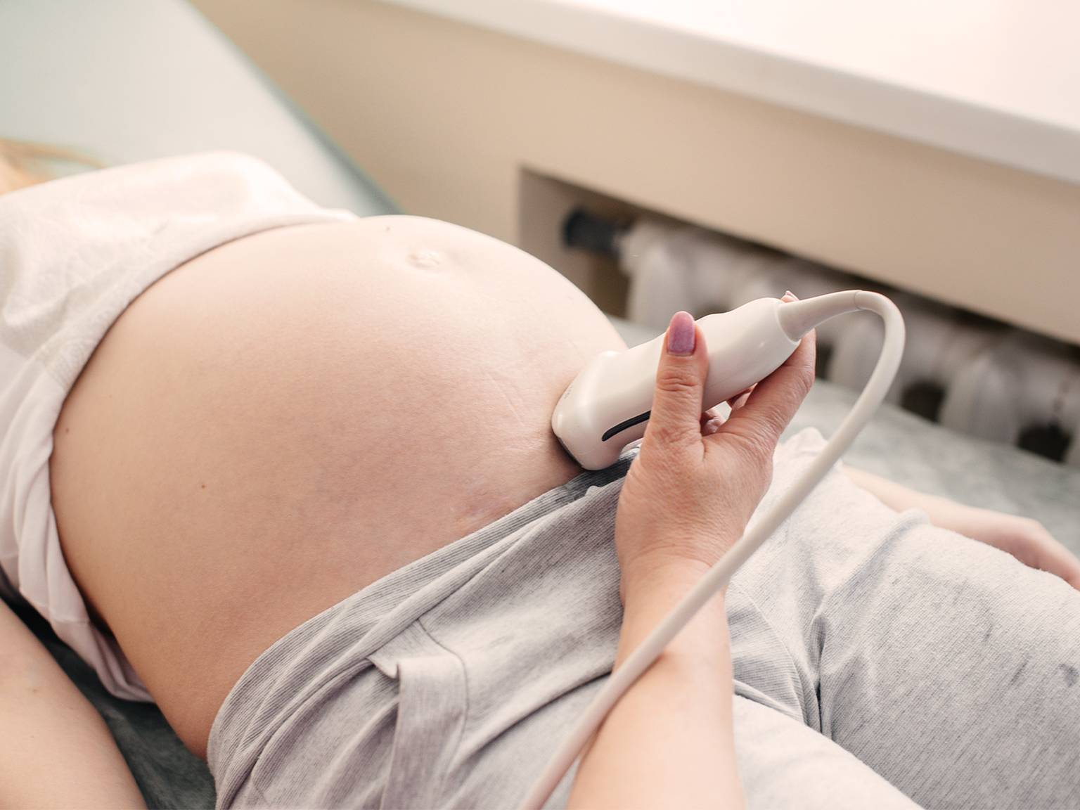 Eine schwangere Person liegt im Liegen und erhält in einer medizinischen Einrichtung eine Ultraschalluntersuchung ihres Bauches.