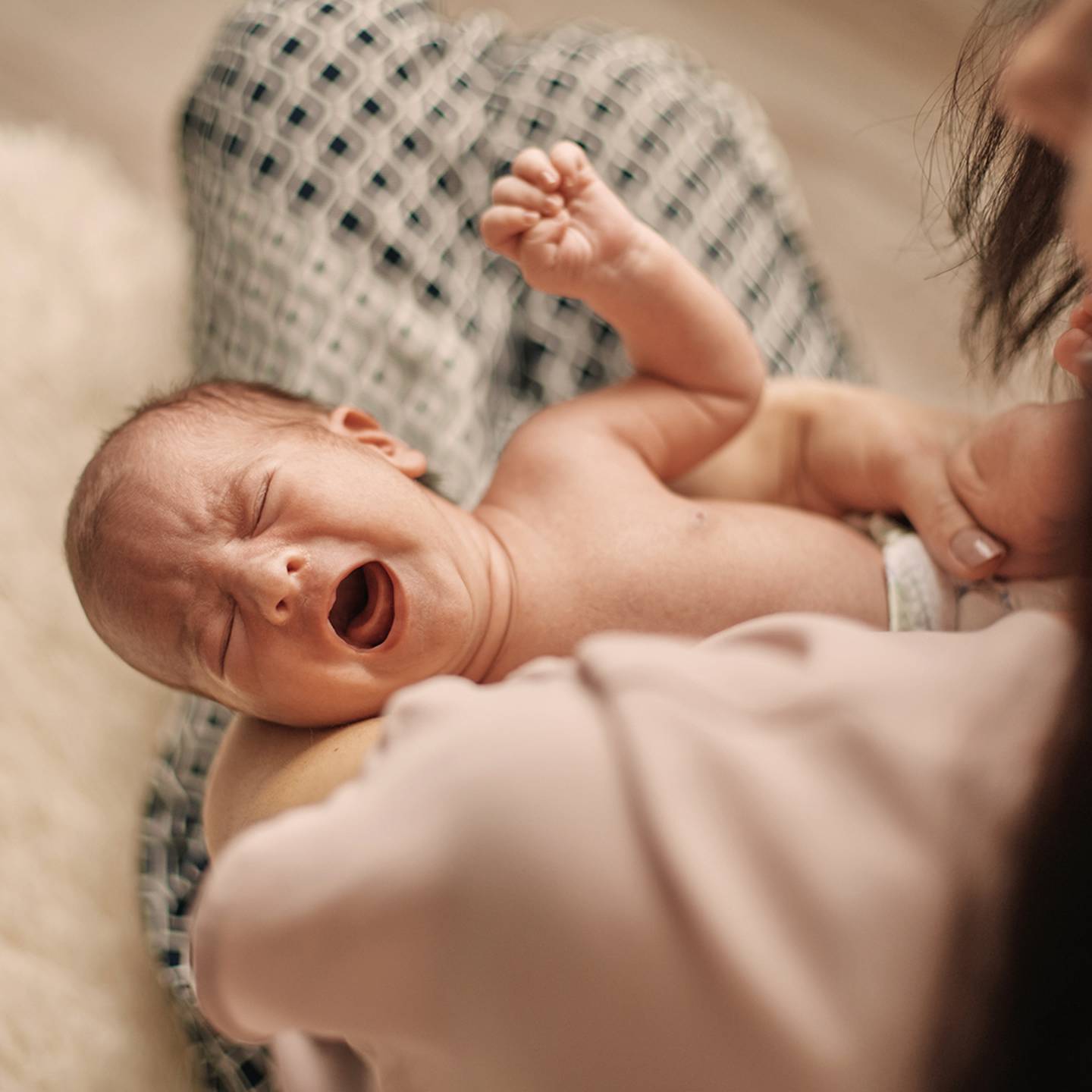 Ein weinendes Baby liegt in den Armen eines Erwachsenen, der eine Windel trägt. Der Erwachsene ist teilweise sichtbar und hält das Baby sanft.