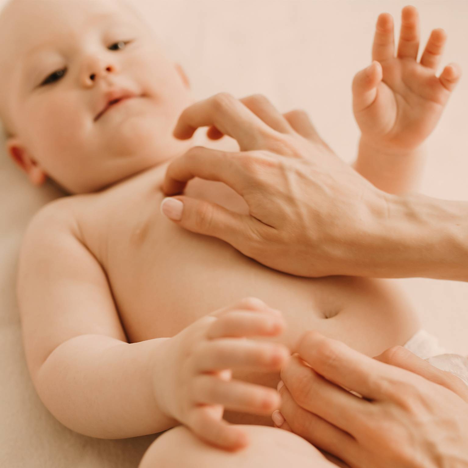 Ein Baby liegt mit freudigem Gesichtsausdruck auf einer weichen Oberfläche und wird sanft von den Händen eines Erwachsenen gekitzelt.