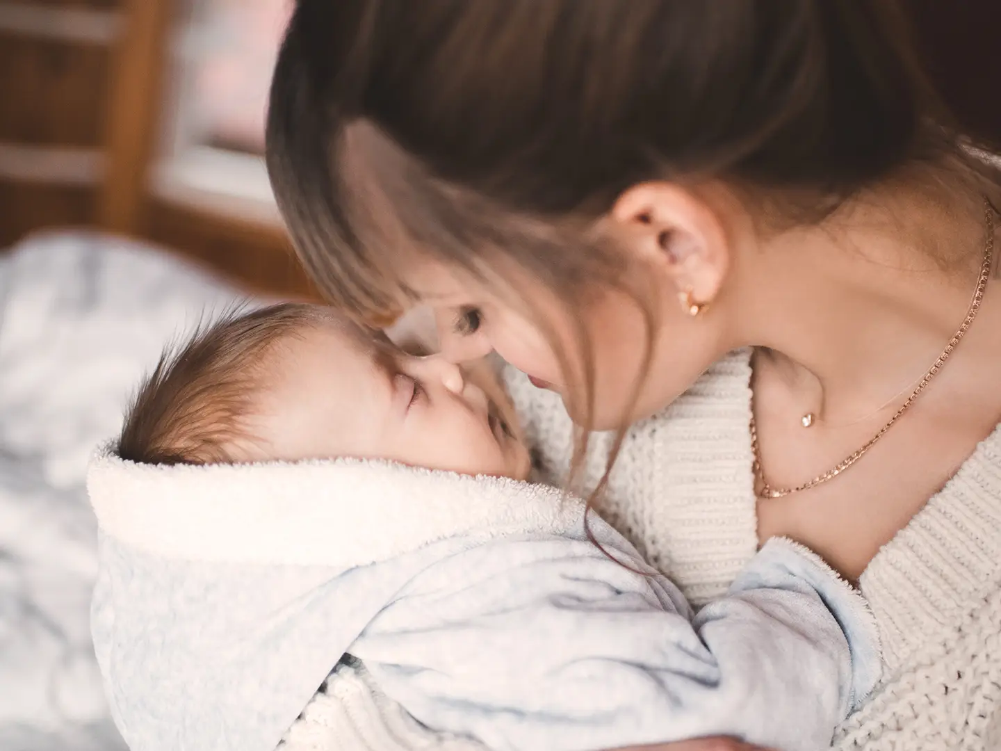 Eine Frau hält sanft ein in eine weiche Decke gewickeltes Baby und teilt einen zärtlichen Moment, in dem sich ihre Nasen berühren.