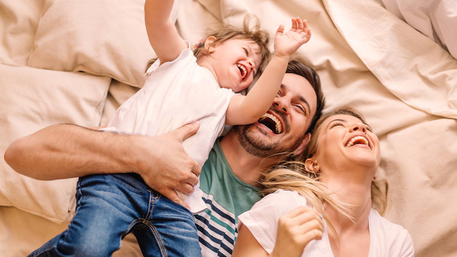 Familie liegt lachend im Bett und tobt