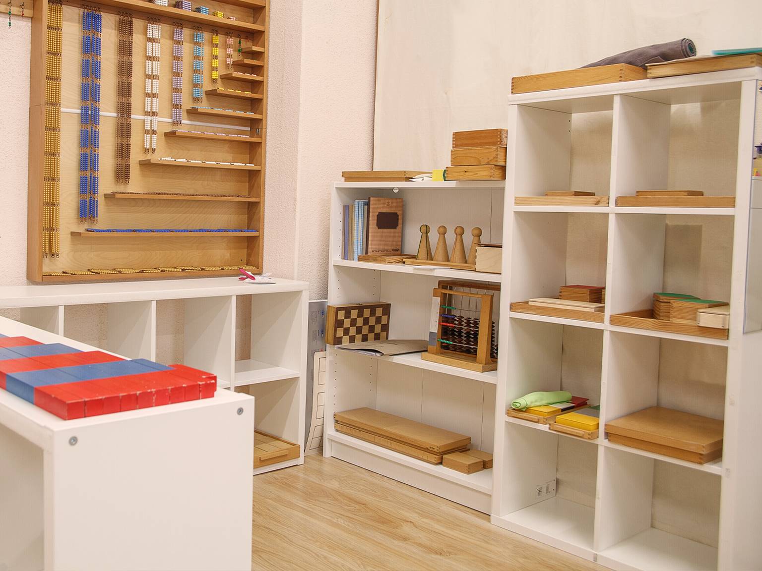 Regale voller Montessori-Lehrmaterialien, darunter Holzklötze, Stäbe und geometrische Formen, in einem Kinderzimmer.