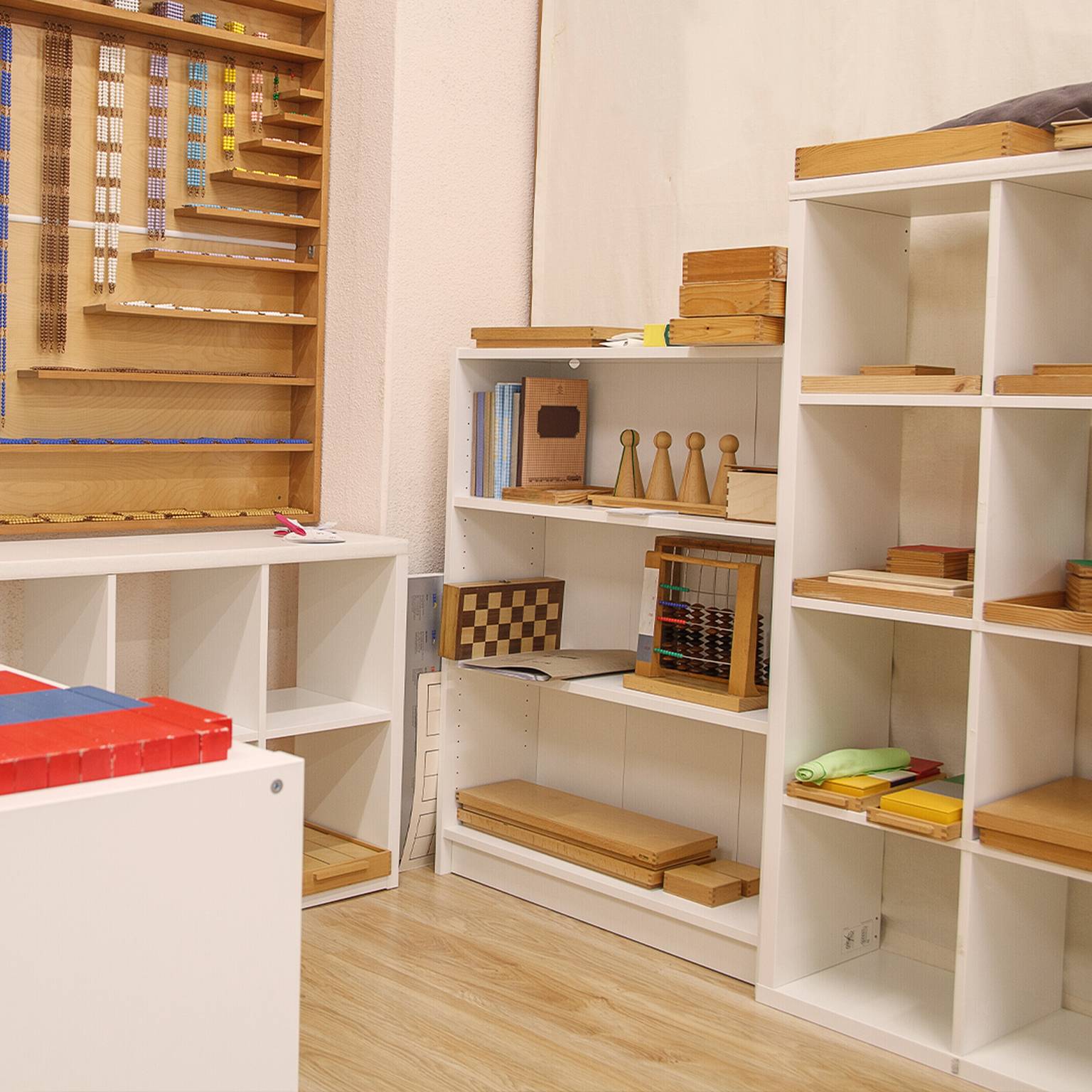 Regale voller Montessori-Lehrmaterialien, darunter Holzklötze, Stäbe und geometrische Formen, in einem Kinderzimmer.