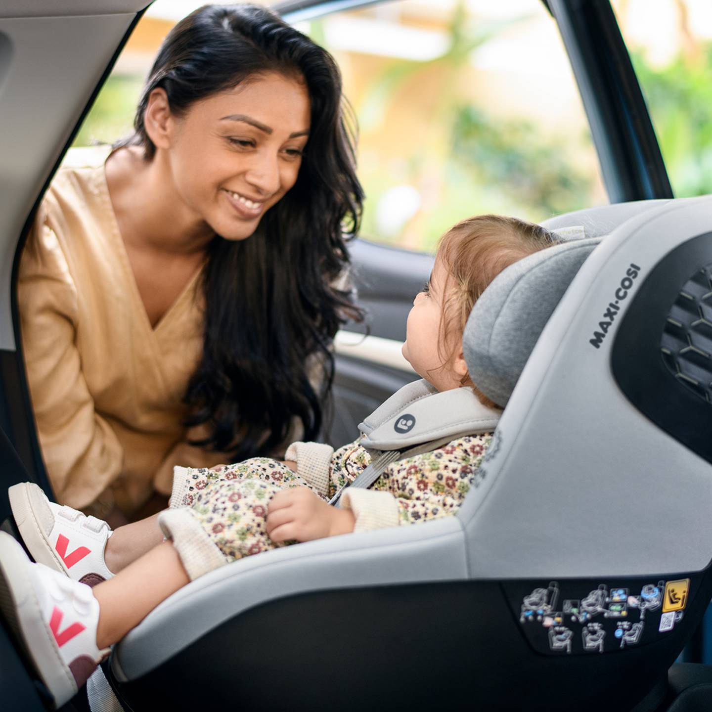 Ein Kind sitzt in einem Kindersitz in einem Auto und schaut eine Frau an.