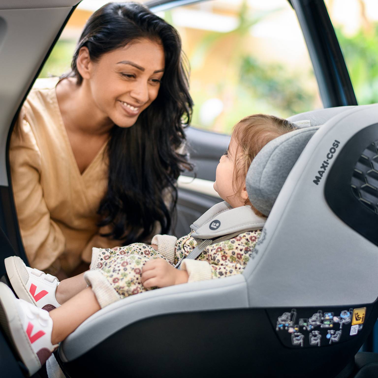Ein Kind sitzt in einem Kindersitz in einem Auto und schaut eine Frau an.