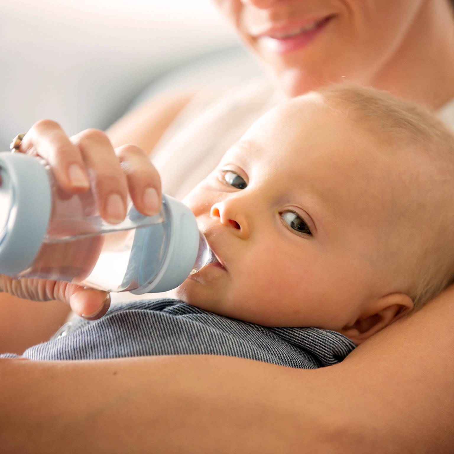 Ein Baby trinkt aus einer Flasche, die von einem Erwachsenen gehalten wird, der lächelt und das Baby in seinen Armen hält.